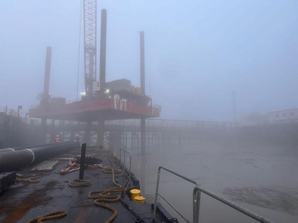 Jack-up platform beside a jetty in early-morning fog