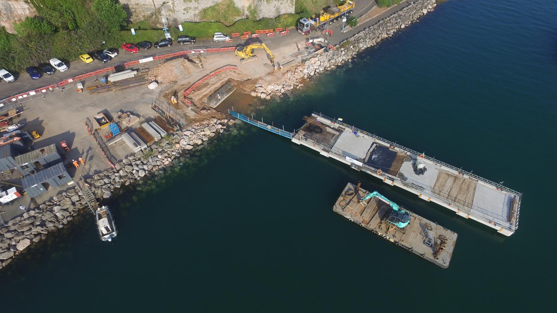 Aerial view of a pontoon under construction beside a work barge and rock armour